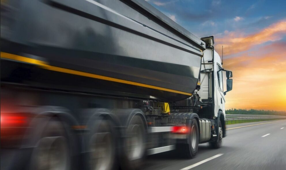 shutterstock_2224435455 Truck huge dump trailer heavy bulk cargo drives fast spinning tire rubber wheels along the evening highway at dusk sunset with motion blur effect
