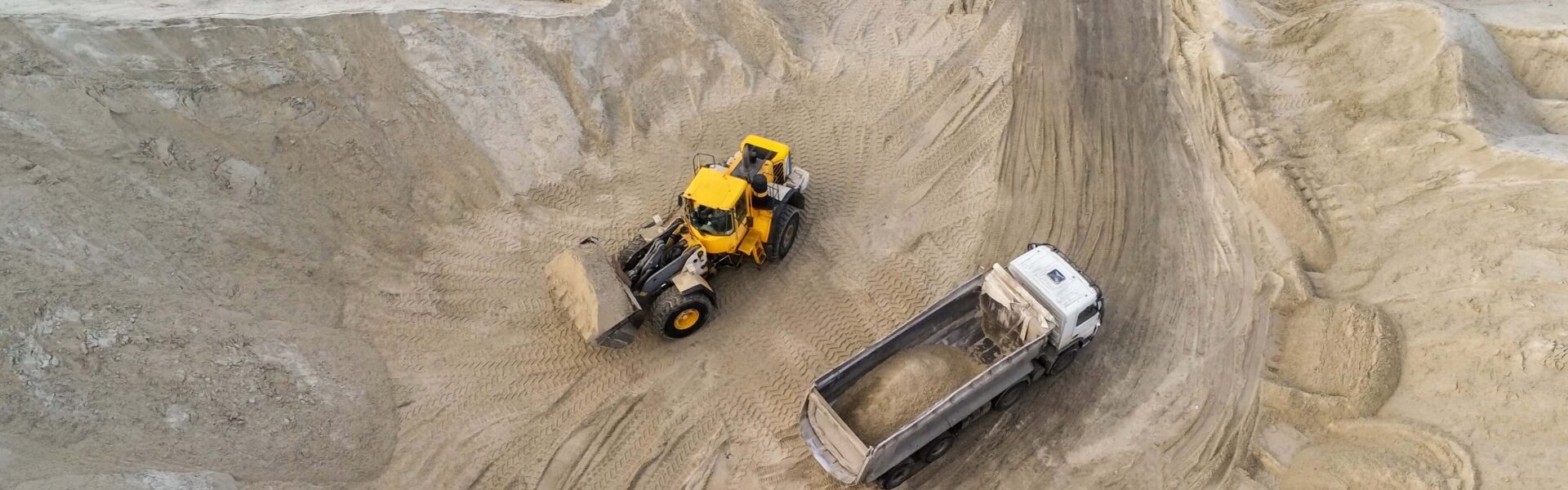 Big heavy wheel loader loading sand into dump truck in sand pit. Heavy industrial machinery concept.